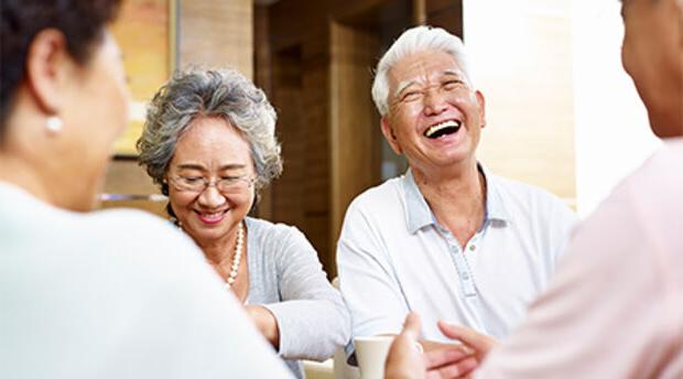 Four older people seated around a coffee table and smiling